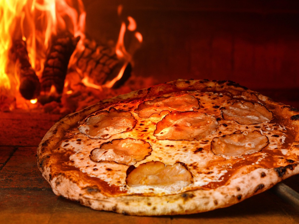 Eine neapolitanische Pizza wird in einen Ofen mit einer brennenden Flamme geschoben.