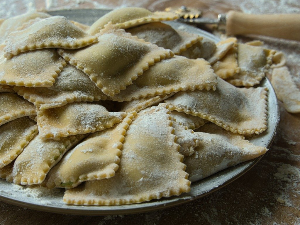Frisch hergestellte Ravioli liegen auf einem Teller bereit, um gekocht zu werden.